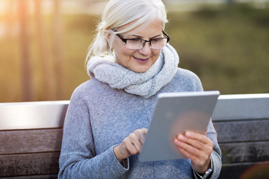 Client Center - Senior Woman Using Digital Tablet Outdoors While Sitting on a Bench